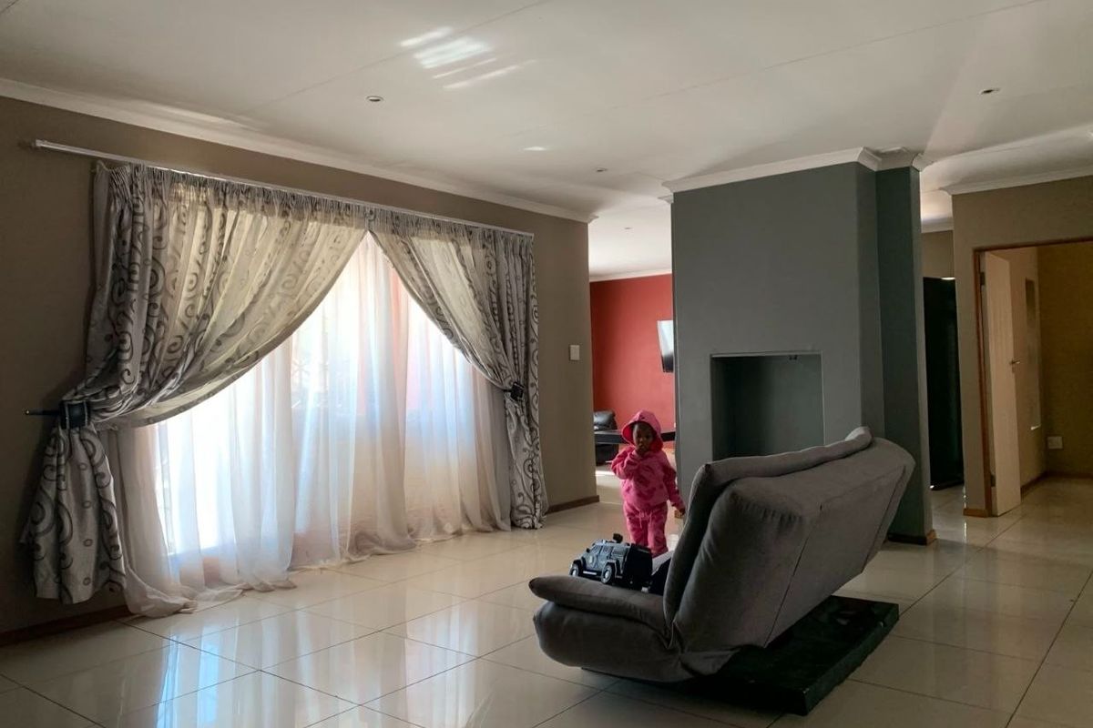 Spacious living room featuring large windows with curtains, tiled flooring, and a central recessed fireplace feature.