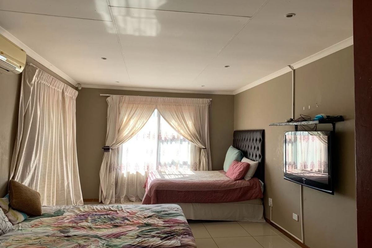 A spacious bedroom featuring tiled flooring, recessed lighting, and an integrated air conditioning unit, with large windows providing natural light.