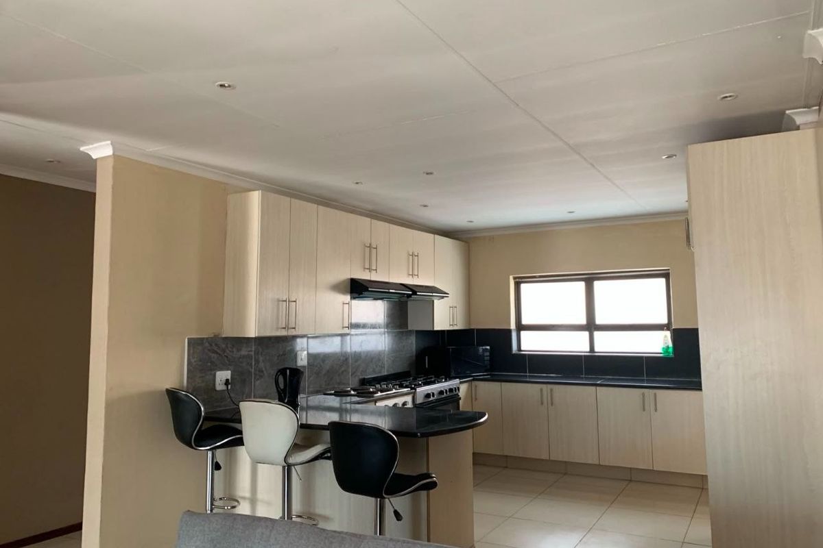 A functional kitchen featuring light wood-finish cabinetry, dark granite countertops, a gas hob with extractor fan, and tiled flooring.