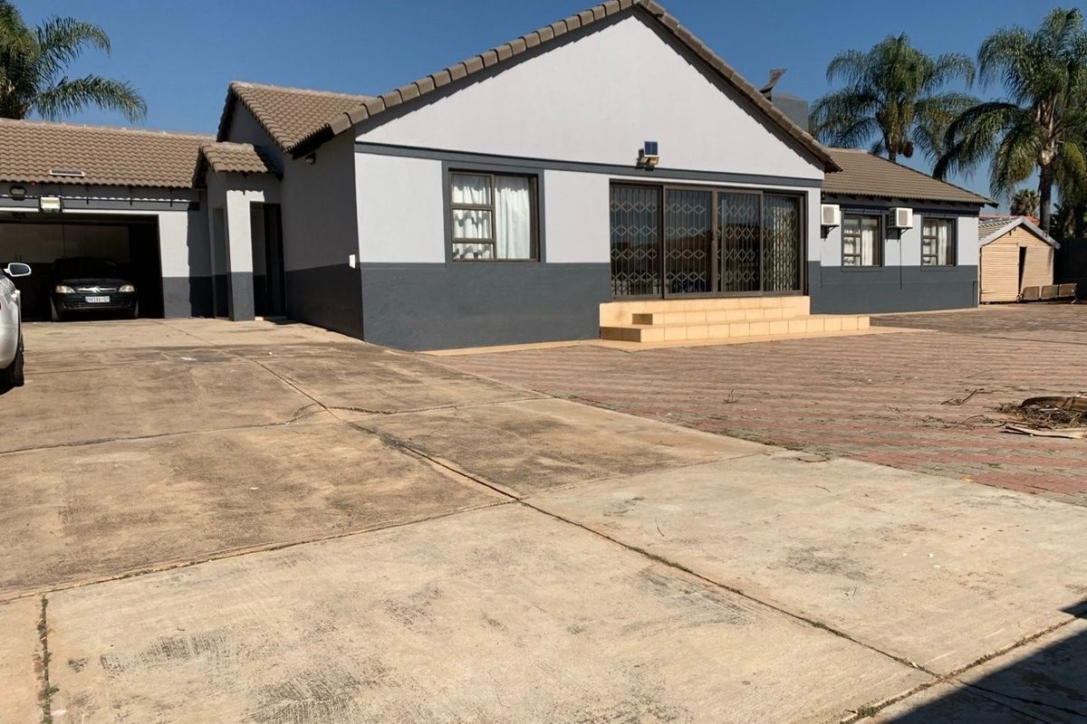Rear view of the house featuring a large concrete driveway, paved patio area, sliding glass doors with security gates, and an attached garage.