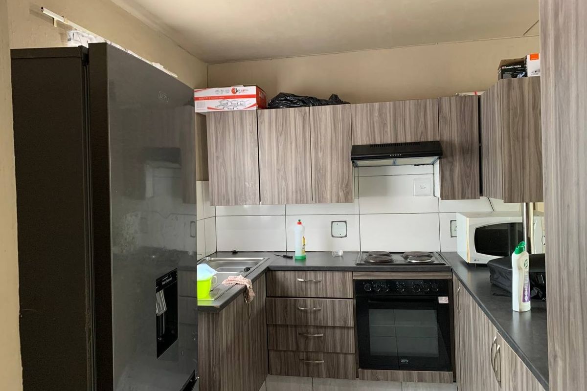 Compact kitchen featuring modern wood-look laminate cabinetry, dark countertops, built-in oven, electric hob, extractor fan, and tiled backsplash.