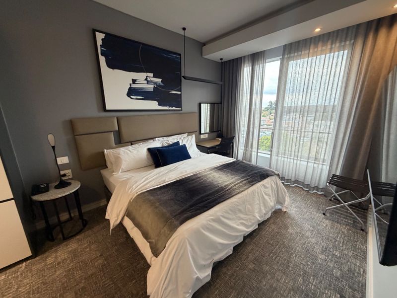 Modern bedroom featuring a built-in desk, upholstered headboard, and floor-to-ceiling windows with natural light and city views.