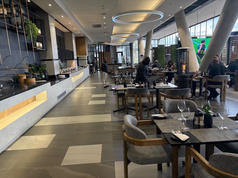 A modern, well-appointed clubhouse dining area featuring contemporary lighting, stone-topped service counters, and large structural concrete columns.