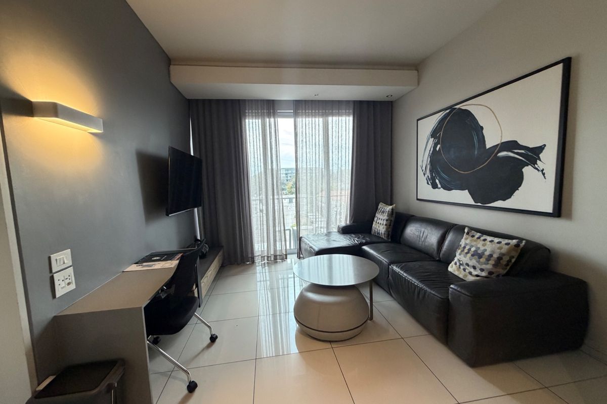 A modern living room featuring tiled floors, a built-in desk, and a sliding glass door leading to a balcony, creating a bright and functional space.