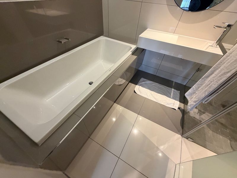 Modern bathroom featuring a sleek built-in bathtub, wall-mounted basin with chrome fixtures, and contemporary large-format wall and floor tiling.