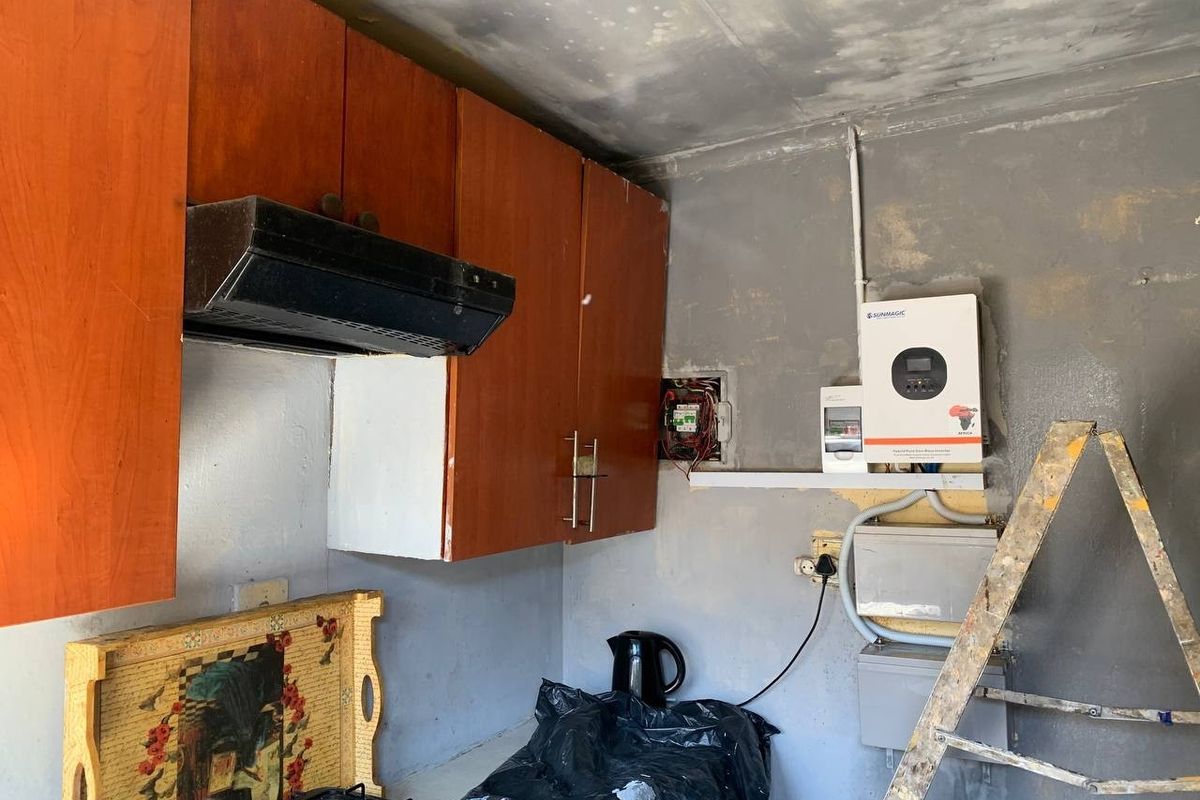 A kitchen area featuring wooden cabinetry and a solar inverter installation, currently requiring significant wall and ceiling repairs and finishing.