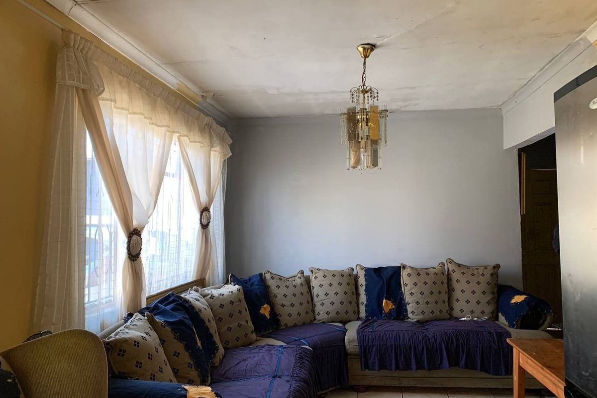 A living room featuring tiled flooring and a decorative chandelier, currently showing signs of wear including ceiling cracks and peeling paint.