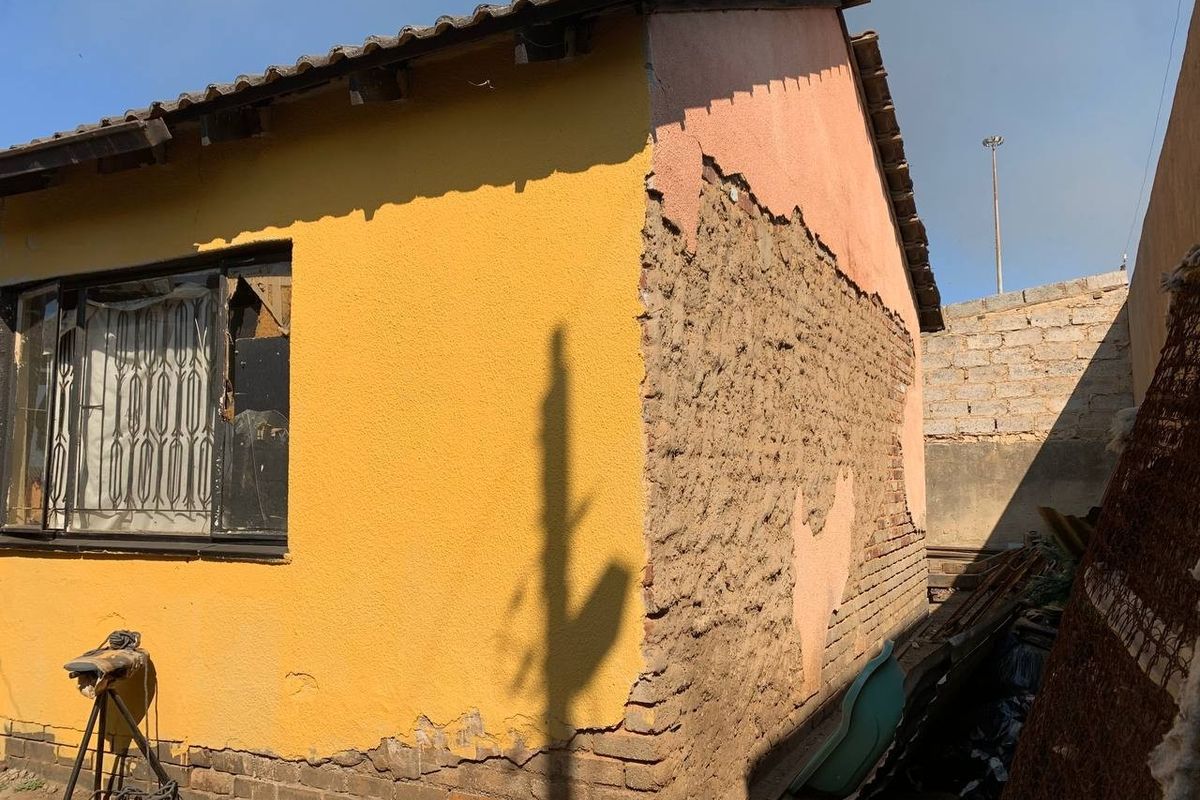 Rear exterior view of a house showing significant deterioration of the exterior wall plaster and masonry, requiring structural repair and maintenance.