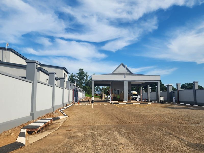 A well-maintained residential estate entrance featuring a modern security gatehouse, paved driveway, and secure perimeter walling.