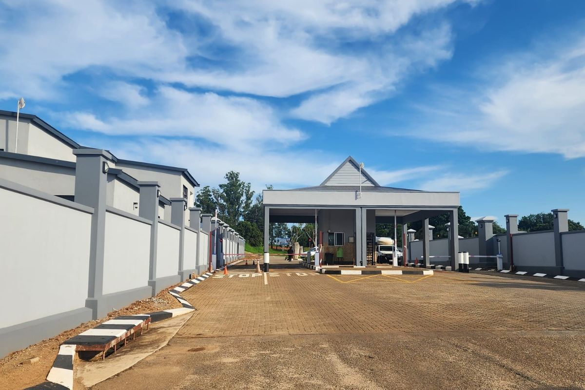 A well-maintained residential estate entrance featuring a modern security gatehouse, paved driveway, and secure perimeter walling.