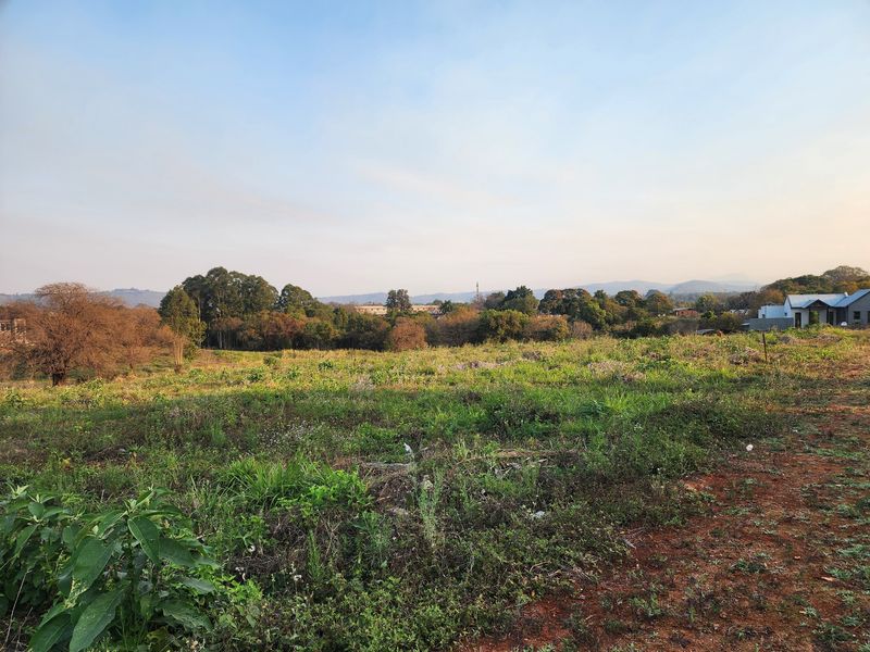 A wide-angle view of an undeveloped residential plot featuring natural vegetation and scenic distant mountain views.