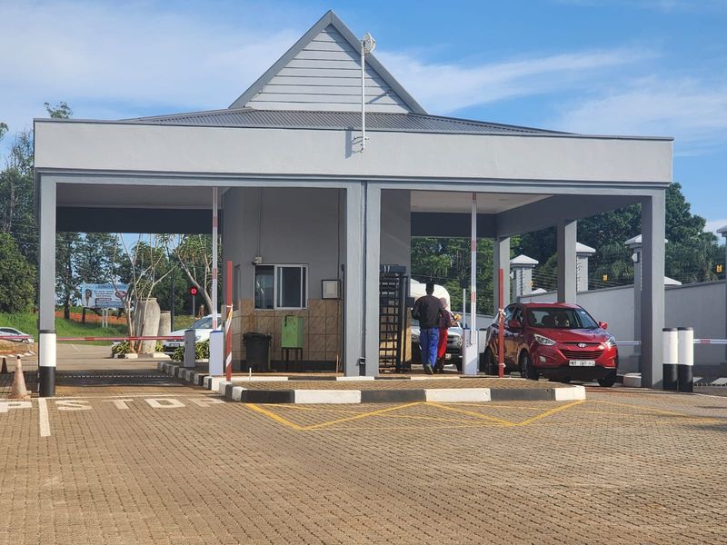 A well-maintained residential estate security gatehouse featuring a paved entrance, boom gate access control, and a structured guard office.