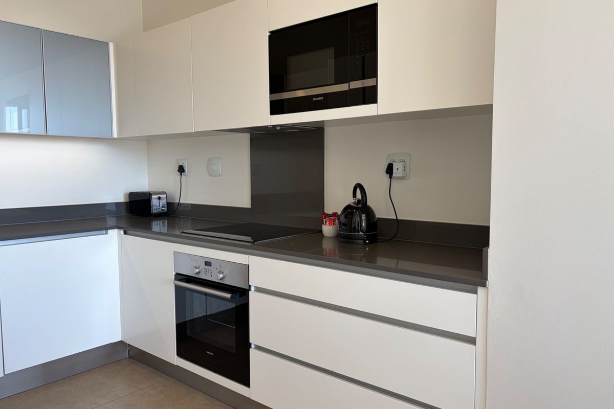 Modern kitchen featuring sleek white cabinetry, stone countertops, integrated oven, hob, and built-in microwave with neutral tiled flooring.