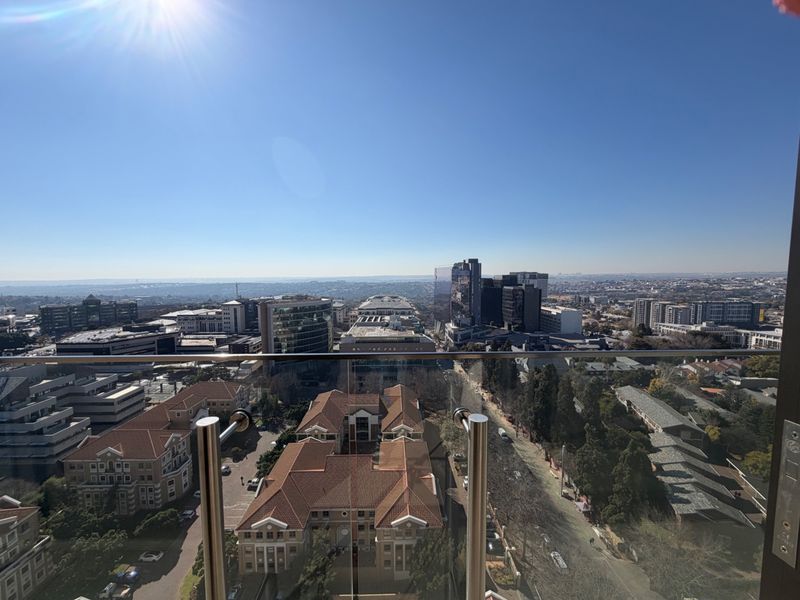 Elevated urban cityscape view captured from a balcony featuring a modern glass balustrade with stainless steel supports.