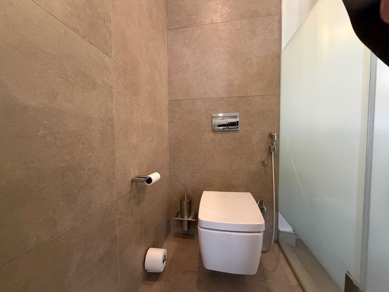 Modern bathroom featuring a wall-mounted toilet with a concealed cistern, bidet spray, and neutral large-format wall tiling.