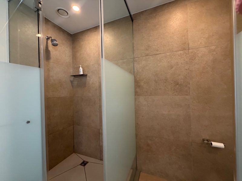 A modern bathroom featuring a spacious walk-in shower with frosted glass enclosure and neutral-toned ceramic wall tiling.