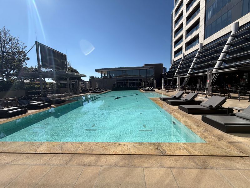 A well-maintained outdoor swimming pool area featuring stone coping and a paved deck, set against a modern apartment building facade.