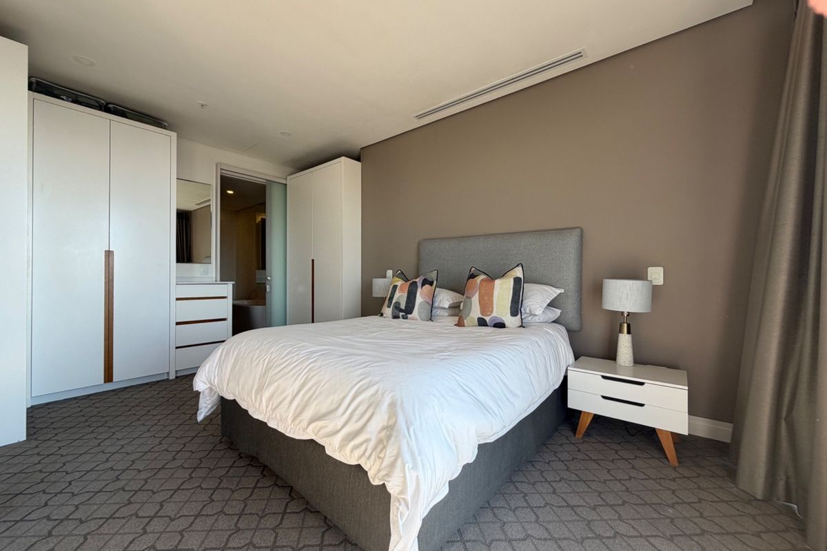 A well-maintained bedroom featuring built-in wardrobes, ducted air conditioning, and neutral carpeted flooring, with an en-suite bathroom visible through the doorway.