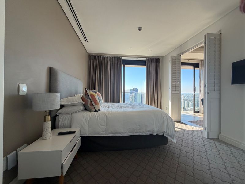 A well-maintained bedroom featuring ducted air conditioning, carpeted flooring, and direct access to a balcony with expansive city views.