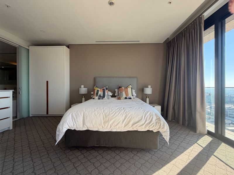 Spacious bedroom featuring built-in wardrobes, ducted air conditioning, and large sliding glass doors opening to a balcony with expansive views.