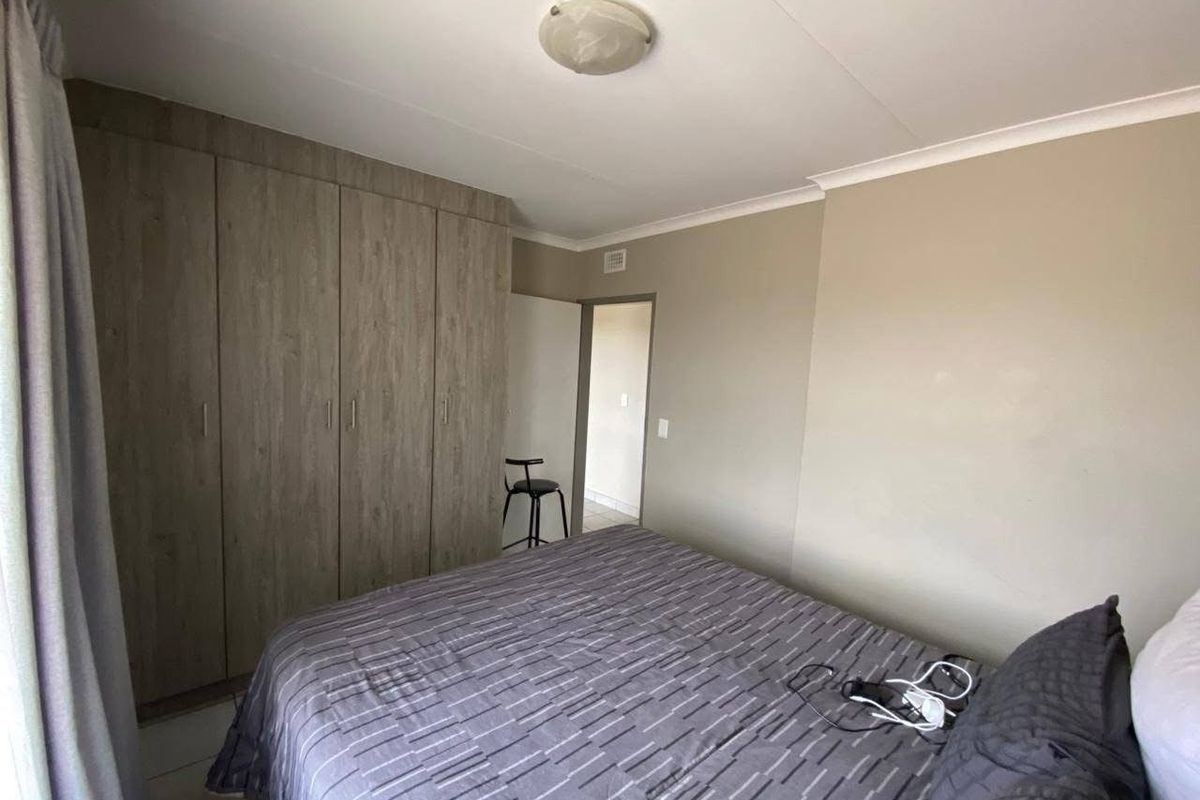 A functional bedroom featuring built-in wooden cupboards, tiled flooring, and neutral wall tones, providing a clean and practical living space.