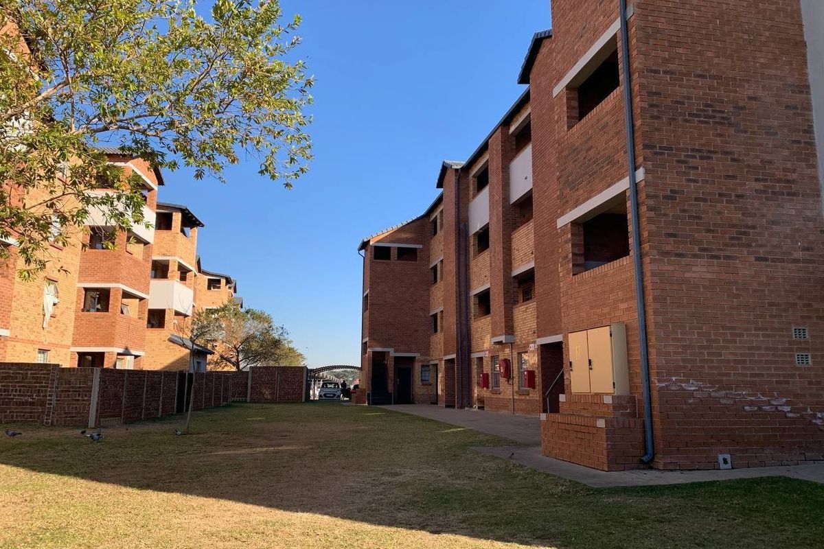 Exterior view of a multi-story apartment complex featuring face brick construction, communal lawn area, and external utility fixtures.