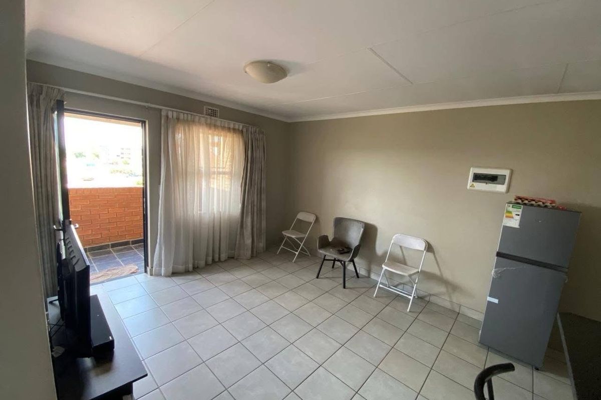A living room featuring tiled flooring, a ceiling light, and a sliding door leading to a balcony, with an integrated electrical distribution board.