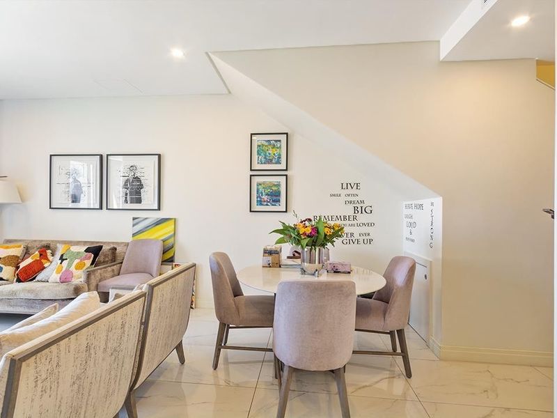 A bright open-plan living and dining area featuring polished marble-look floor tiles, recessed lighting, and a staircase leading to the upper level.