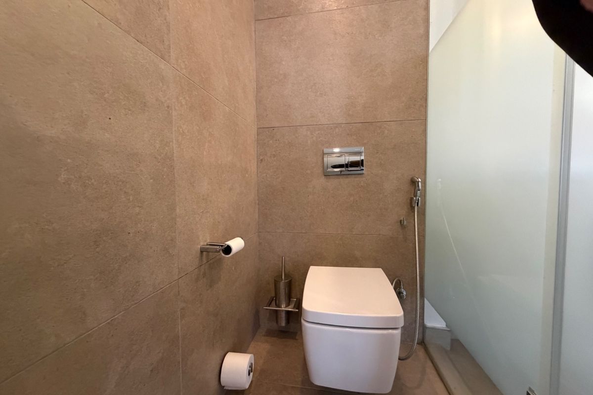 Modern bathroom featuring a wall-mounted toilet with a concealed cistern, bidet spray, and neutral large-format wall tiling.