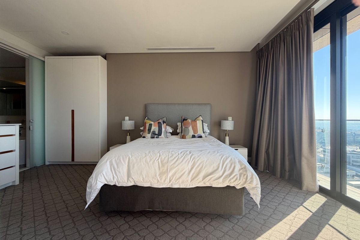 Spacious bedroom featuring built-in wardrobes, ducted air conditioning, and large sliding glass doors opening to a balcony with expansive views.