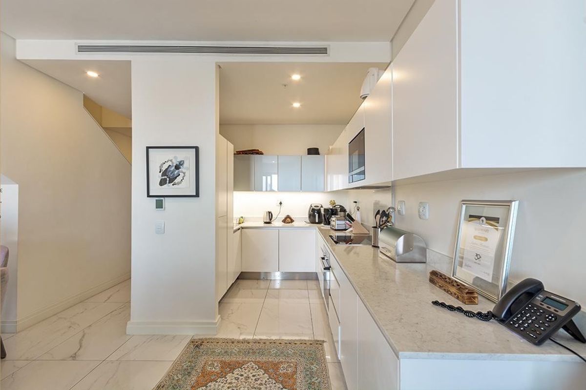Modern kitchen featuring sleek white cabinetry, stone countertops, integrated appliances, and high-quality porcelain floor tiles with recessed lighting.