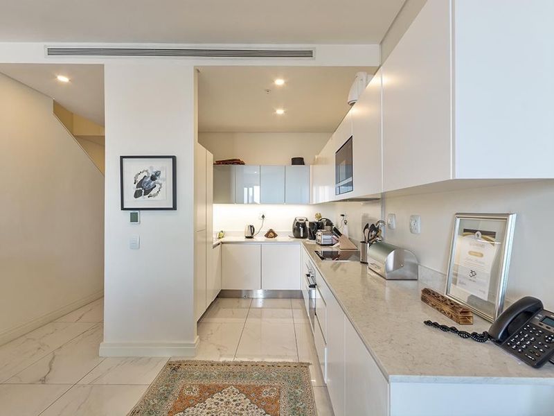 Modern kitchen featuring sleek white cabinetry, stone countertops, integrated appliances, and high-quality porcelain floor tiles with recessed lighting.