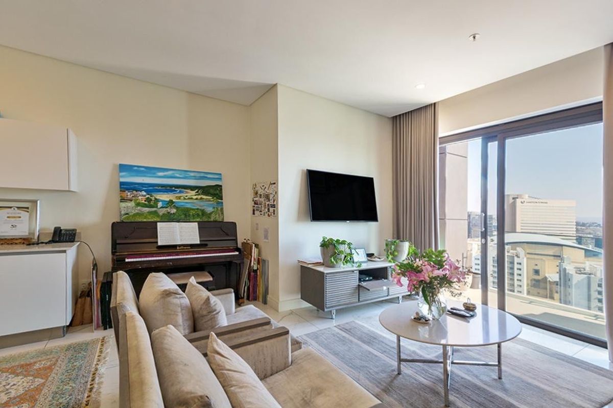 A bright and modern living room featuring tiled floors, recessed lighting, and large sliding glass doors that open to a balcony with city views.