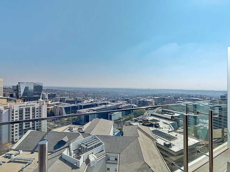 Elevated panoramic city view captured from a modern apartment balcony featuring a sleek glass and stainless steel balustrade.