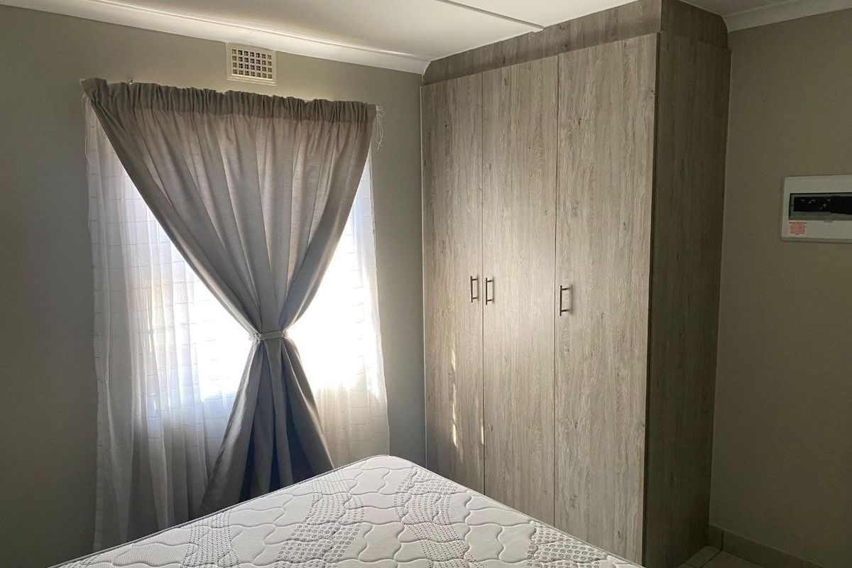 A bedroom featuring built-in wood-look cupboards, a ventilation grille, and an electrical distribution board.