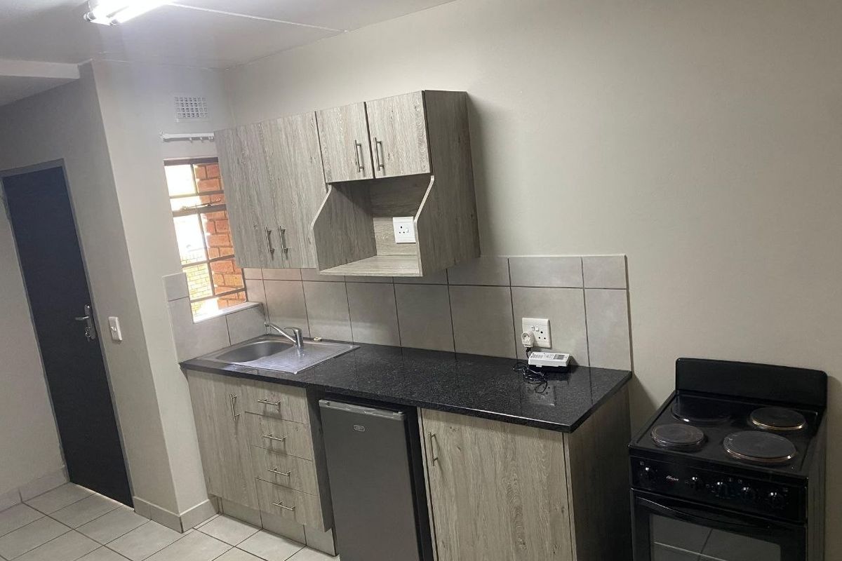 A compact, functional kitchen featuring modern laminate cabinetry, granite countertops, a stainless steel sink, and a freestanding electric stove with tiled flooring.