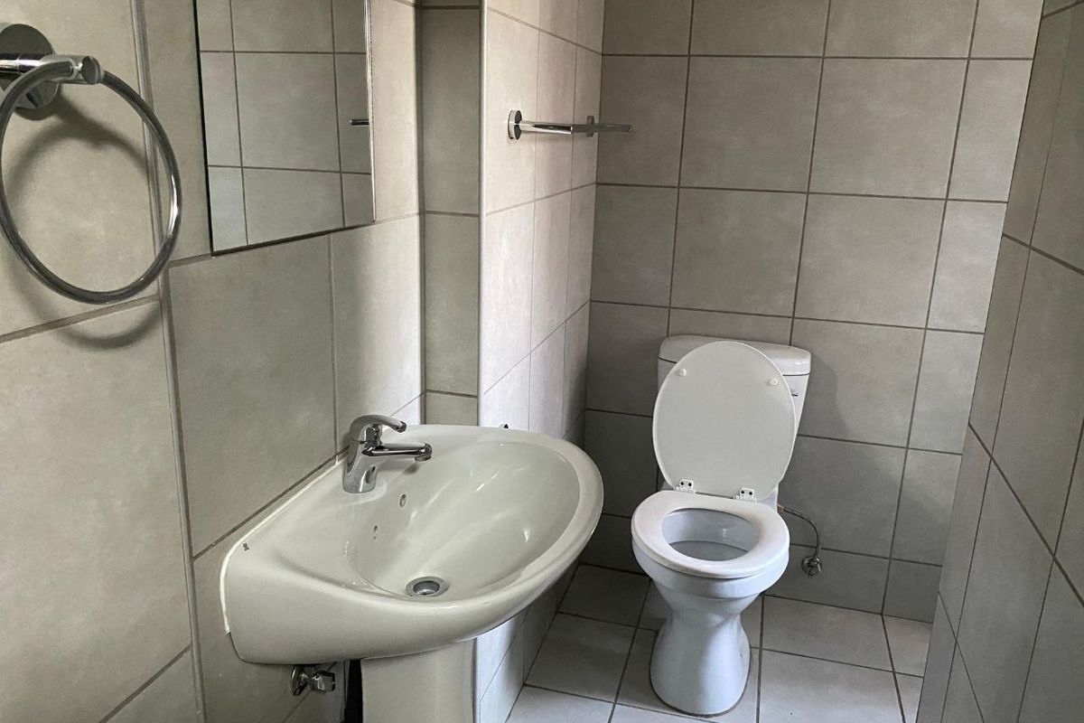 A functional bathroom featuring a pedestal basin, toilet, and neutral wall and floor tiling.