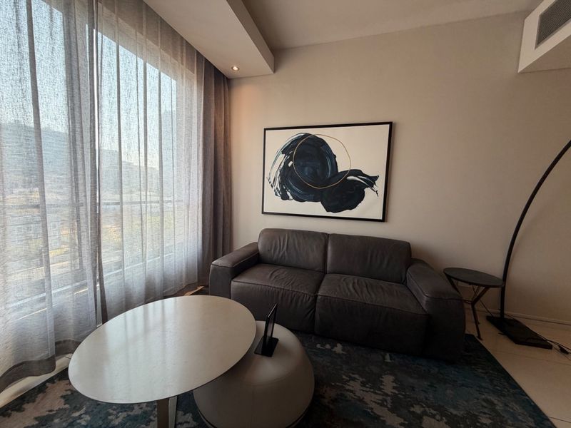 A modern living room featuring large floor-to-ceiling windows with sheer curtains, recessed ceiling lighting, and integrated ducted air conditioning.