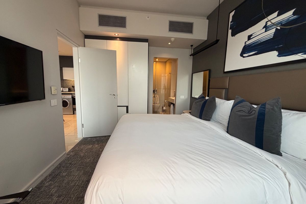 Modern bedroom featuring built-in wardrobes, ducted air conditioning, and direct access to an en-suite bathroom with contemporary finishes.