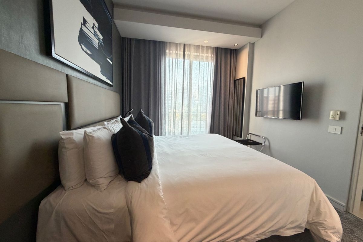 A well-maintained bedroom featuring a large upholstered headboard, wall-mounted television, and floor-to-ceiling curtains providing natural light.
