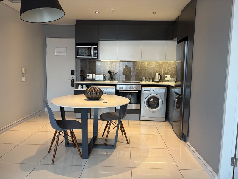Modern open-plan kitchen featuring sleek two-tone cabinetry, integrated appliances, stone splashback, and polished floor tiles in a contemporary apartment setting.