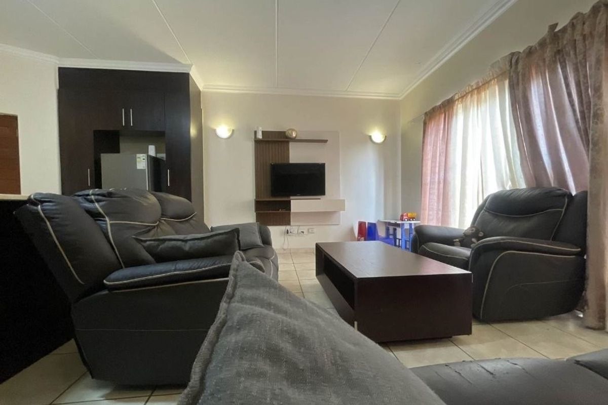 Open-plan living area featuring tiled flooring, coved ceilings, and a built-in media unit, seamlessly connecting to the kitchen space.