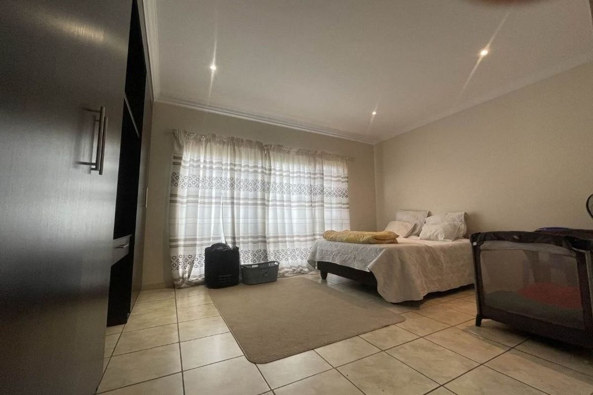 Spacious bedroom featuring tiled flooring, built-in cupboards, and recessed downlighting, offering a functional and neutral living space.
