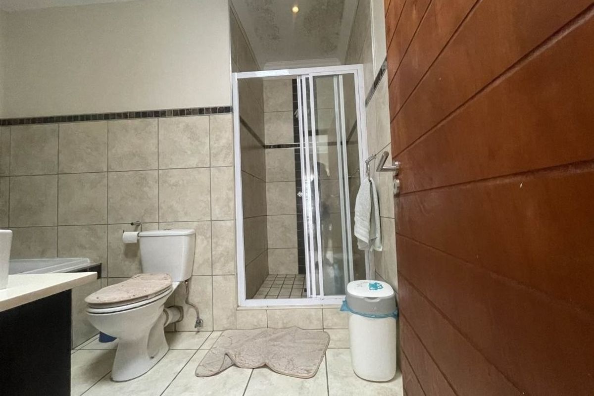 A functional bathroom featuring a shower enclosure, toilet, and tiled finishes, showing signs of ceiling water damage requiring maintenance.