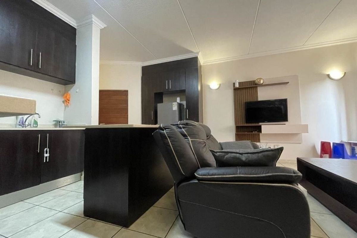 Open-plan living area featuring a modern kitchen with dark cabinetry, a central island, and a built-in media unit in the lounge space.