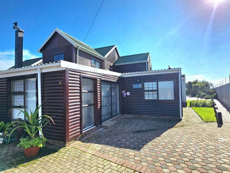 Front exterior view of a townhouse featuring timber-look cladding, a paved driveway, and secure perimeter walling with electric fencing.