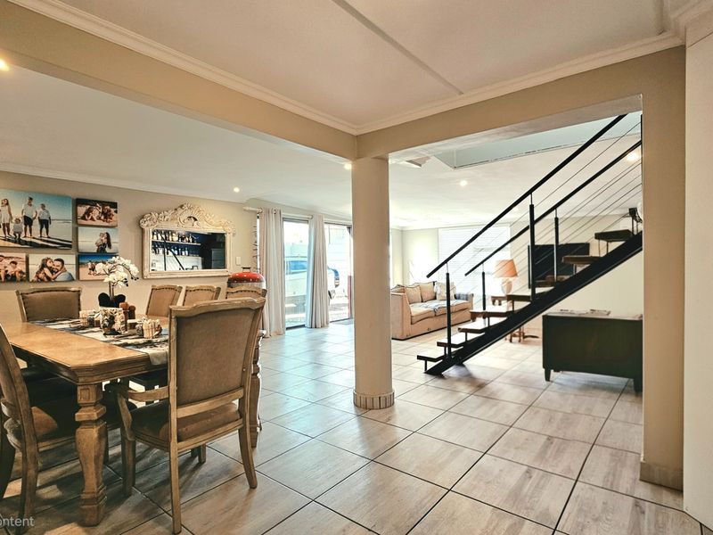 Spacious open-plan living and dining area featuring tiled flooring, a modern staircase, and direct access to the outdoor space through sliding glass doors.