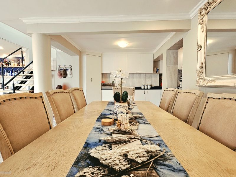 An open-plan dining area featuring a central dining table, adjacent kitchen cabinetry, and a staircase leading to the upper level.