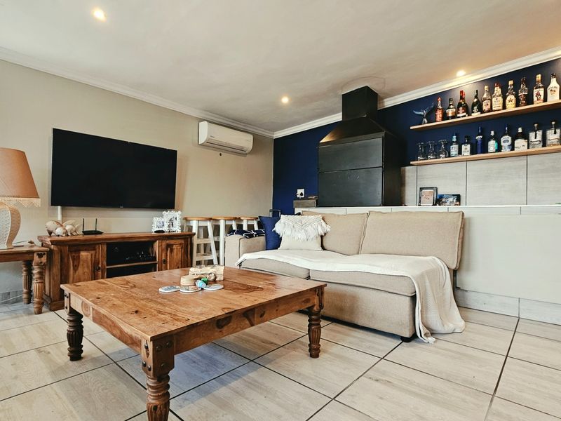 A comfortable living room featuring a built-in fireplace, split-system air conditioning, tiled flooring, and decorative floating shelving against a feature wall.