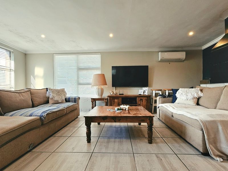 A comfortable living room featuring tiled flooring, recessed downlighting, a split-system air conditioner, and a fireplace chimney breast.